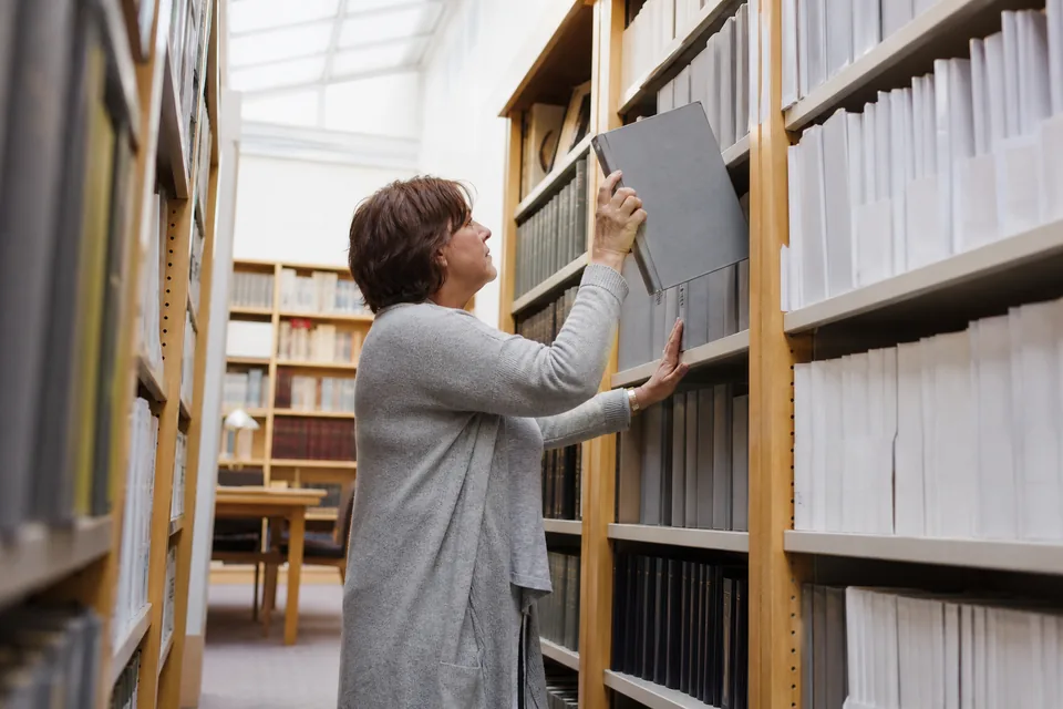 Researcher pulling a binder from library shelves
